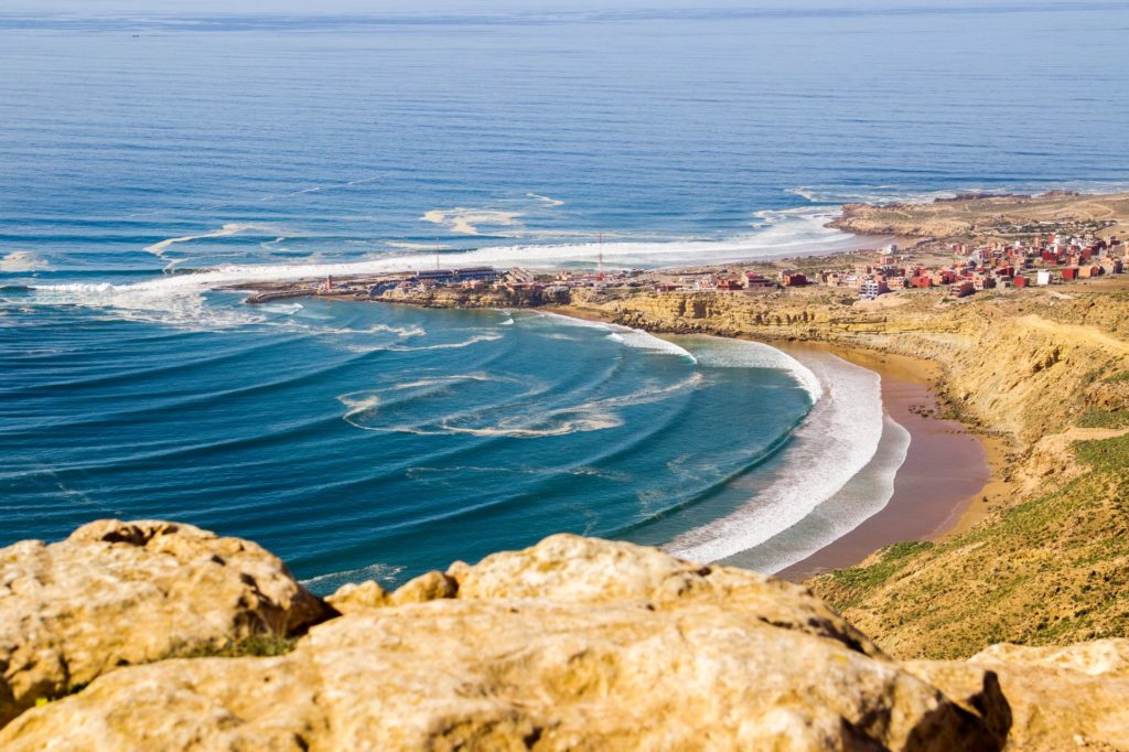 Gentle waves in the bay of Imsouane, Morocco, with the picturesque coastal landscape in the background.