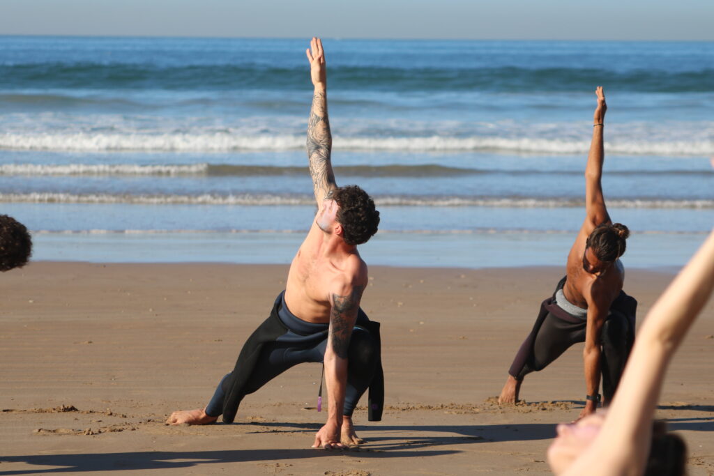 People doing yoga stretches before surfing on the beach in Morocco