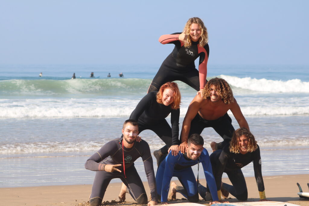 Group of smiling surfers and yogis on the beach after a surf session at Crocro Beach, Morocco