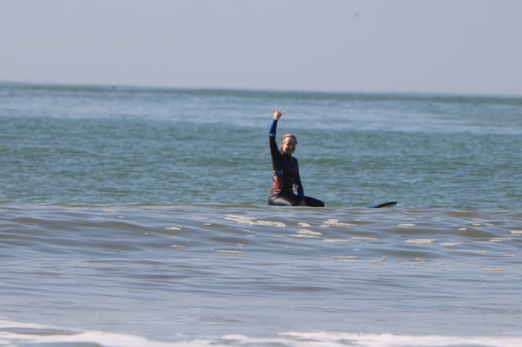 urferin sitzt auf ihrem Board und macht das Shaka-Zeichen am Surfspot in Agadir, Marokko