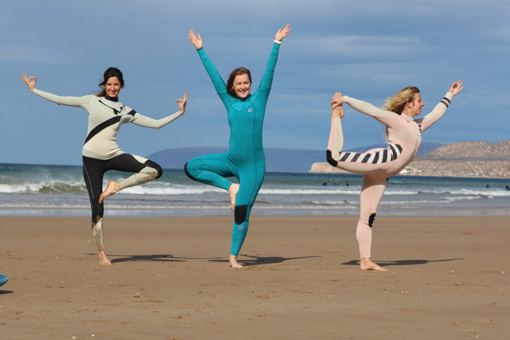 Des clients d'Azul Guesthouse faisant une pose de yoga sur la plage après l'échauffement avant la session de surf.