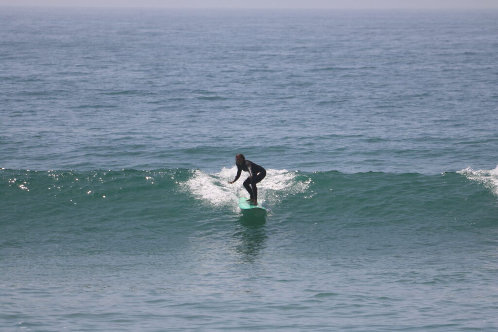 Une surfeuse attrape une vague au large de la côte d'Agadir, au Maroc, avec un ciel bleu et des vagues claires en arrière-plan.