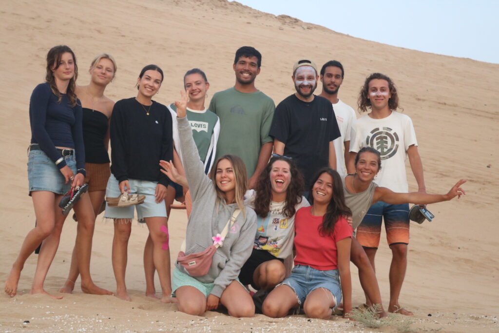 A group of surfers from Azul Guesthouse posing together in the Tamri dunes after an adventurous sand-surfing session at sunset.