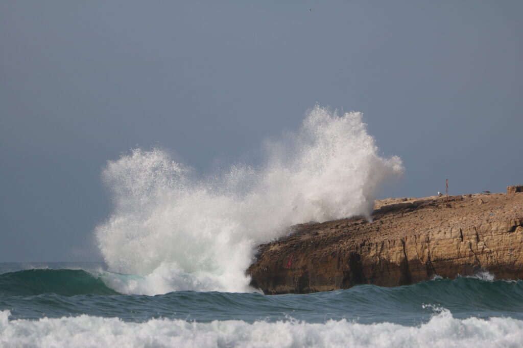 Une vague droite impressionnante à Camel Point, avec de l'eau éclaboussant les rochers et des embruns volant dans les airs, capturant la beauté brute du spot.